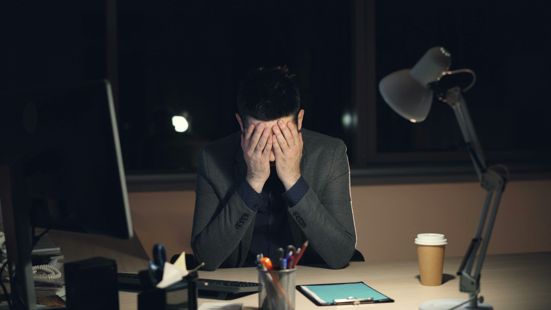 Man in suit sits at desk, head in hands